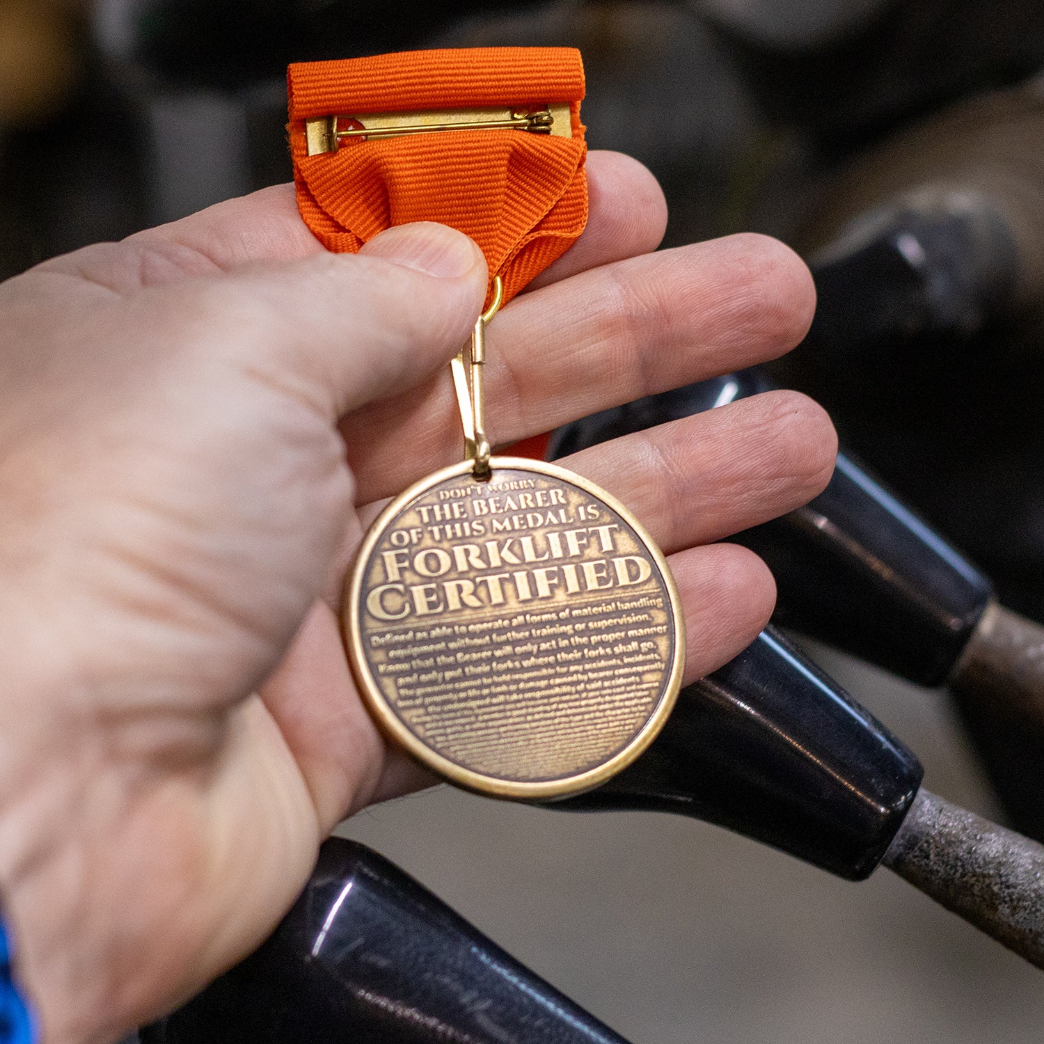 Hand holding reverse side of brass Forklift Certified medal