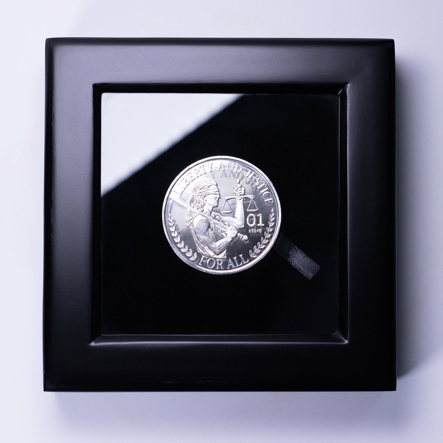 Silver Liberty and Justice coin displayed in a black, glass-topped display box