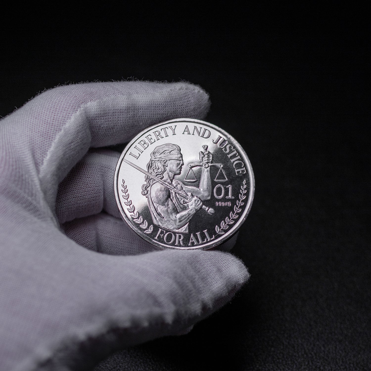 Gloved hand holding silver Liberty and Justice for All coin against a black background