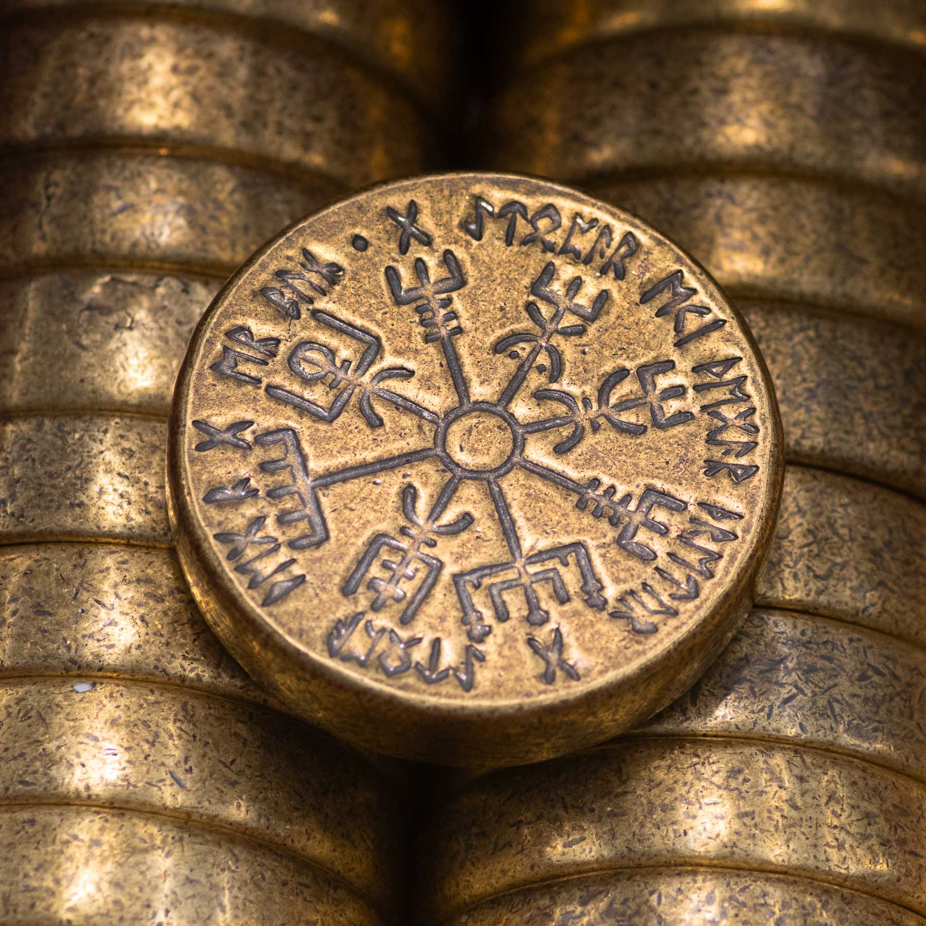A large bronze cast vegvisir rests on top of multiple rows of other cast vegvisir