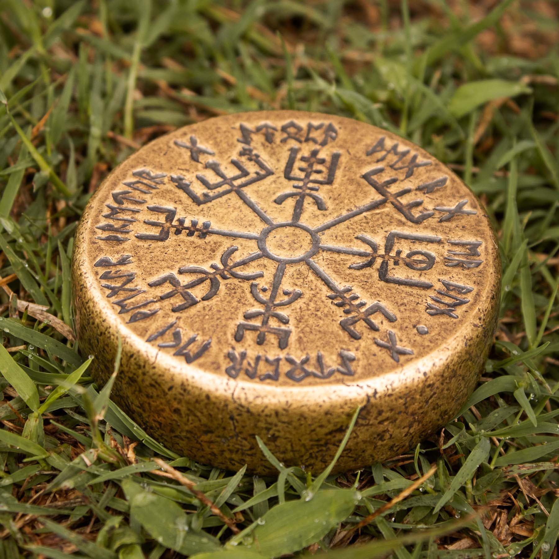 a vegvisir rune in bronze sitting on the ground in the grass