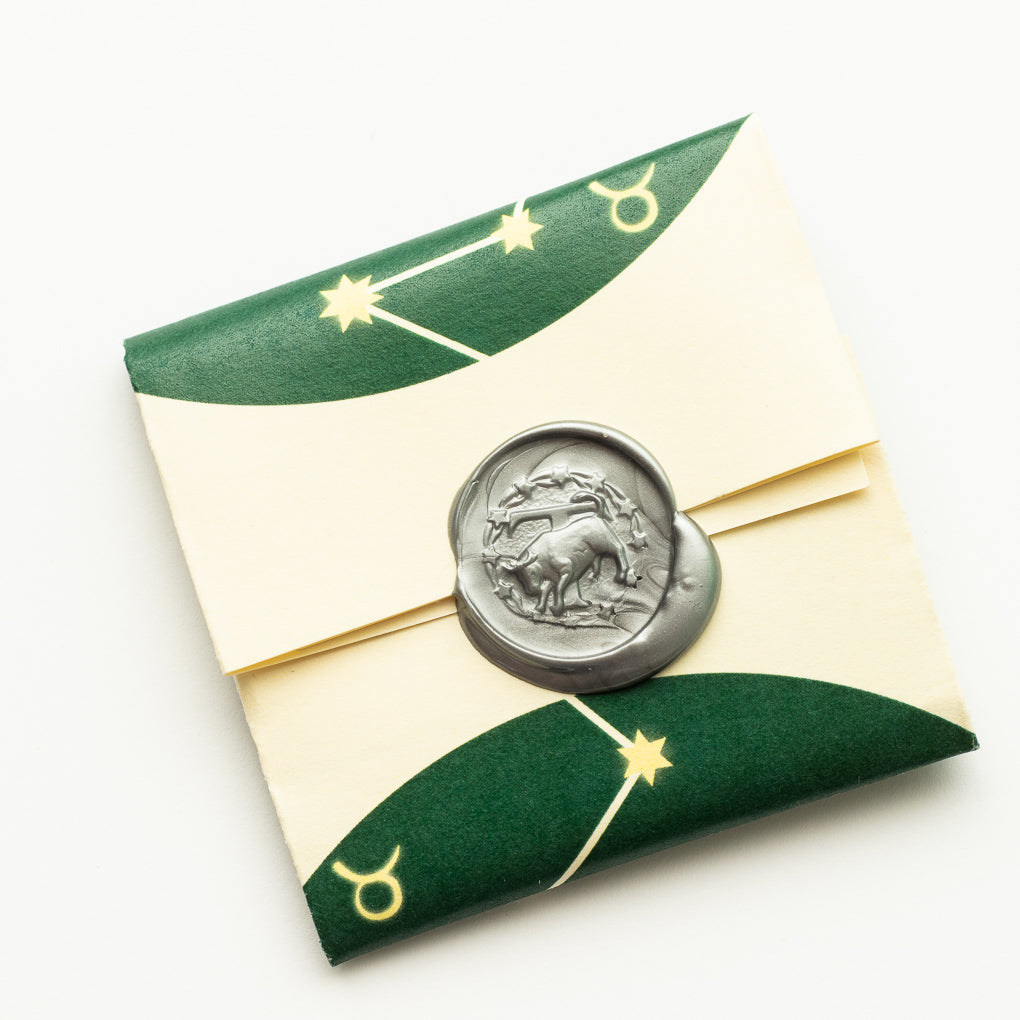Reverse side of Shire Post Mint two-sided Silver Zodiac Taurus Moon Charm packaged in paper foldy with wax seal
