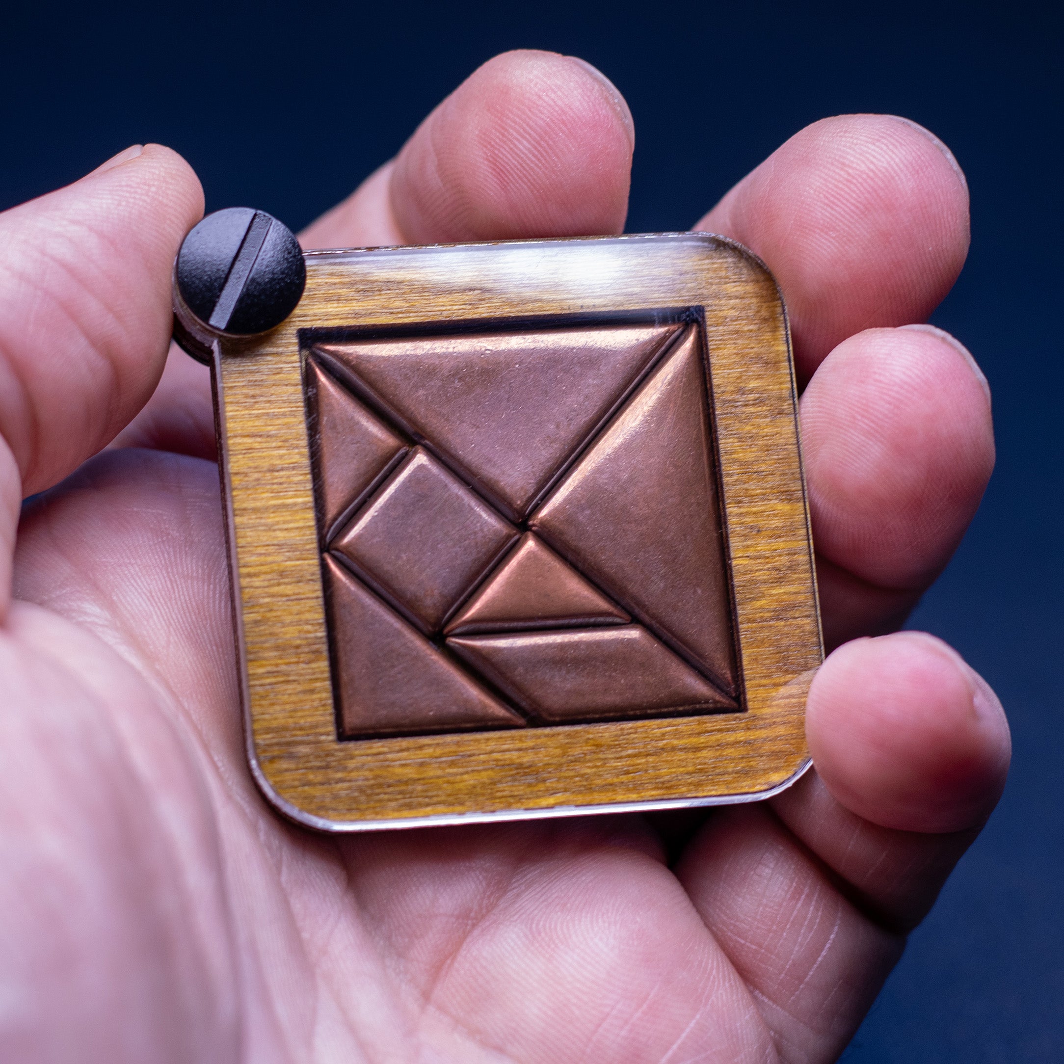 Hand holding Shire Post Mint's solid copper Tangram puzzle completed and in box 