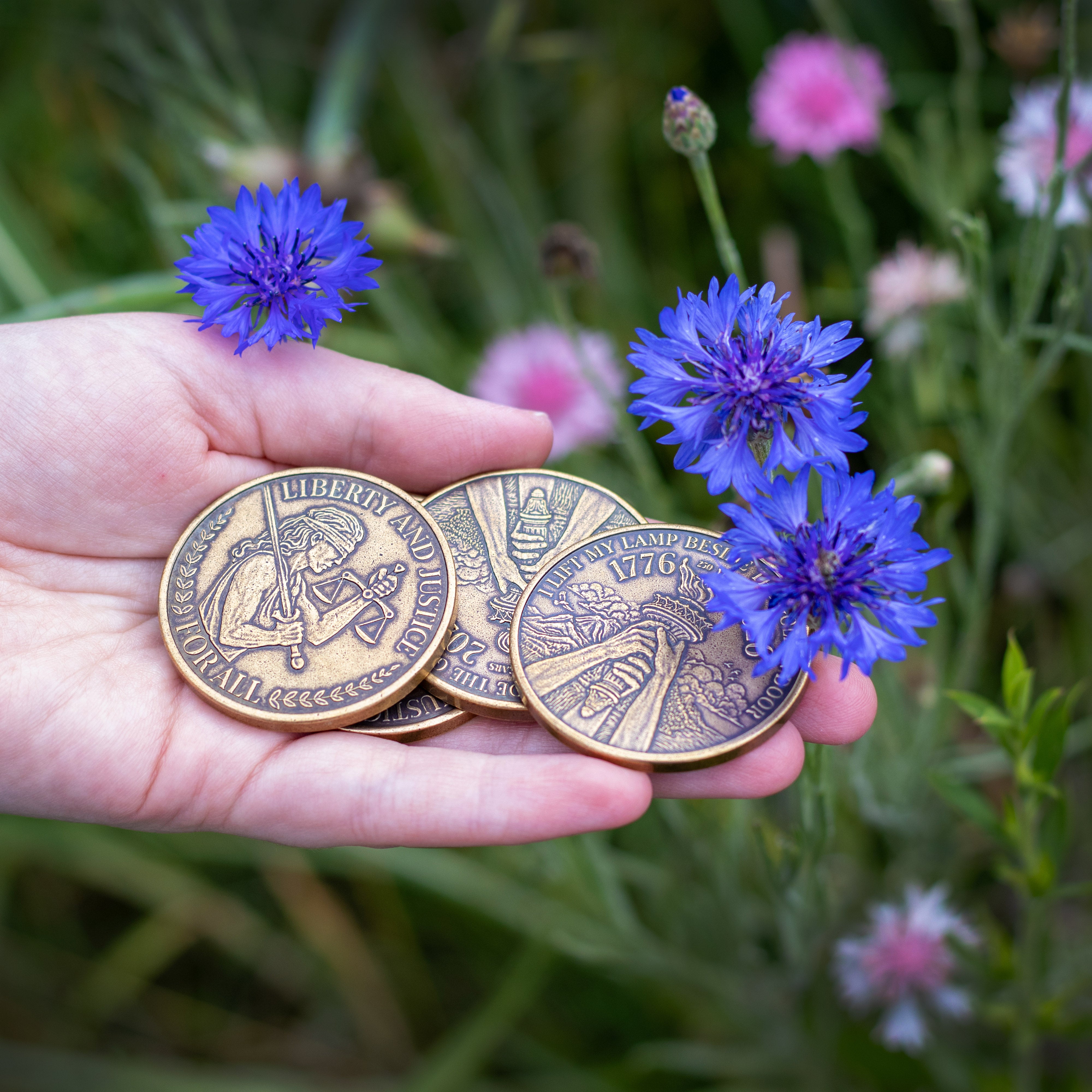 Hand holding stack of Liberty and Justice coins next to blue flowers