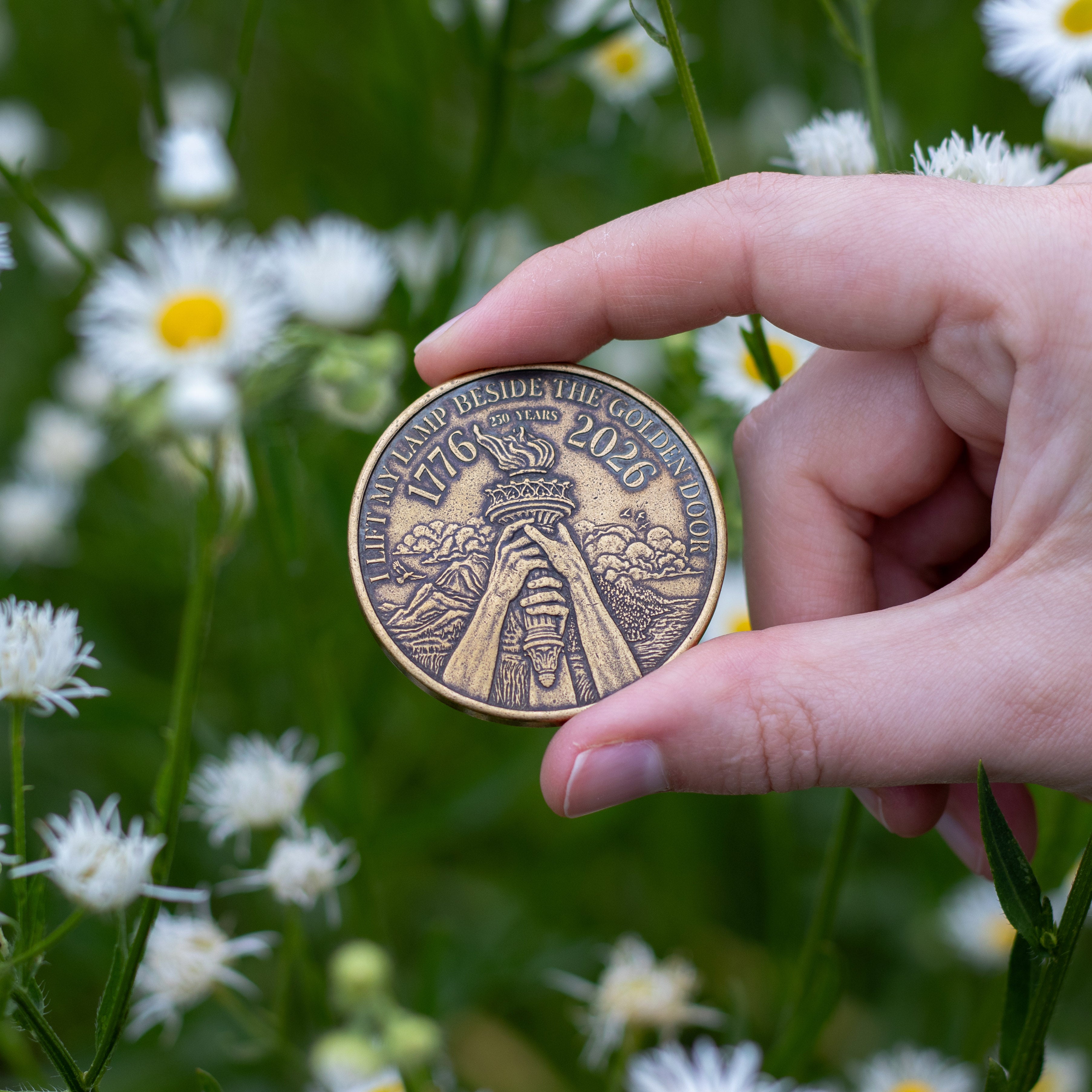 Hand holding reverse of Liberty and Justice coin next to white flowers