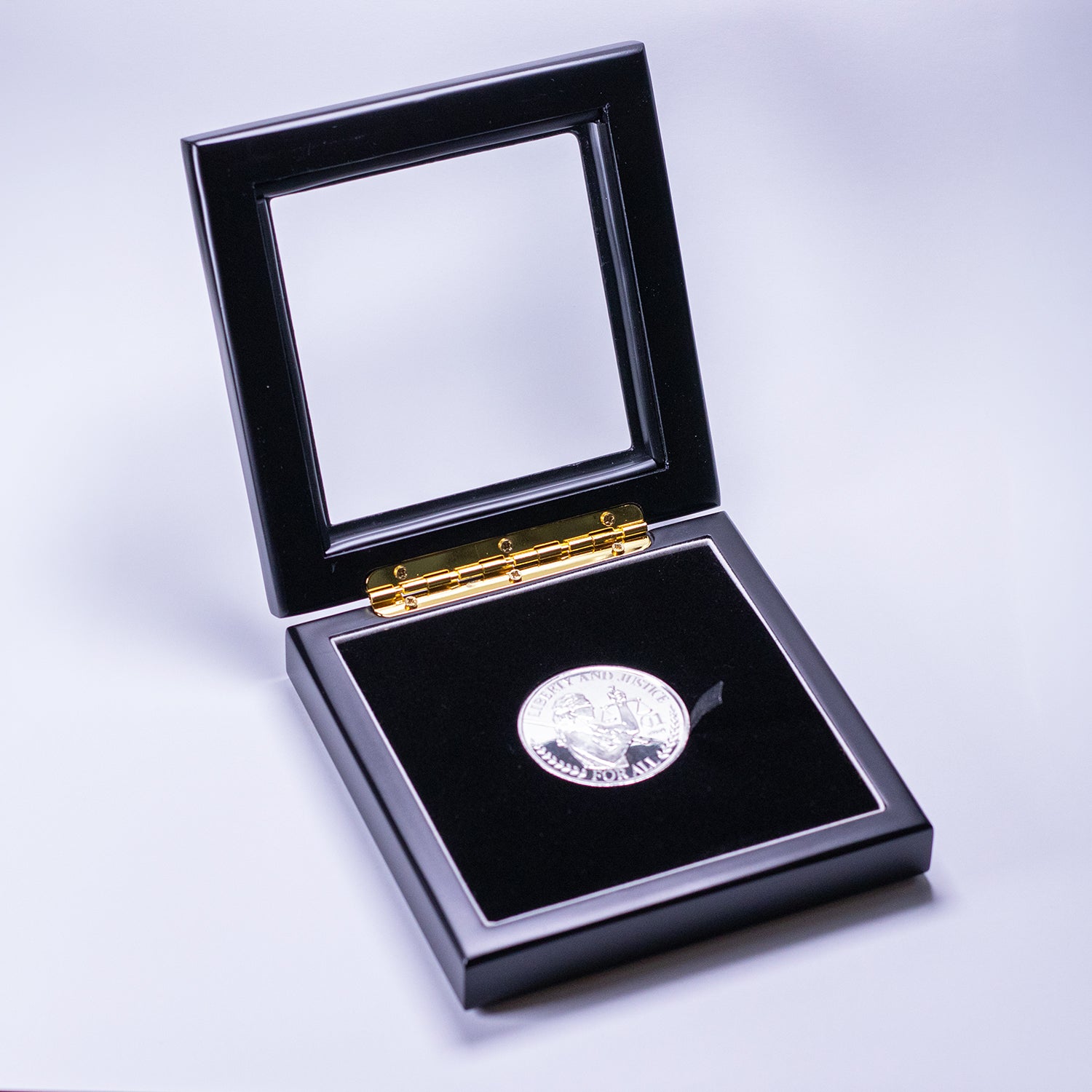 Glass-topped black display box holding the silver Liberty and Justice coin 