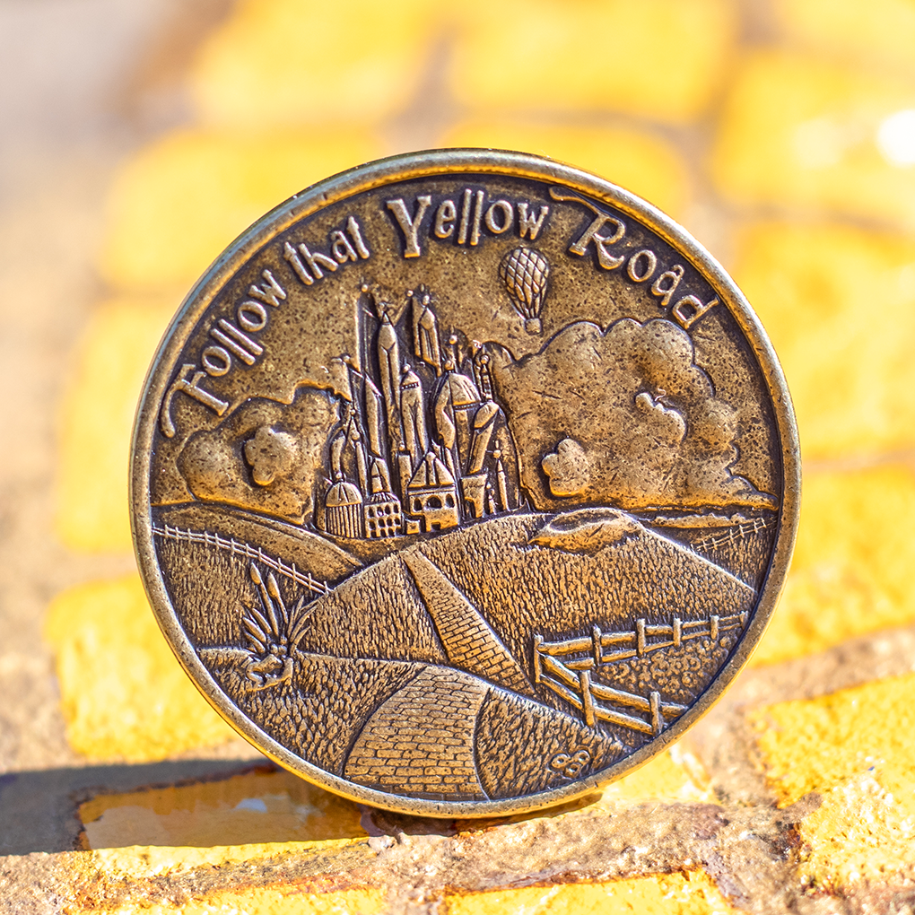 Brass coin with text, 'Follow that Yellow Road' displayed on a hand painted yellow brick road
