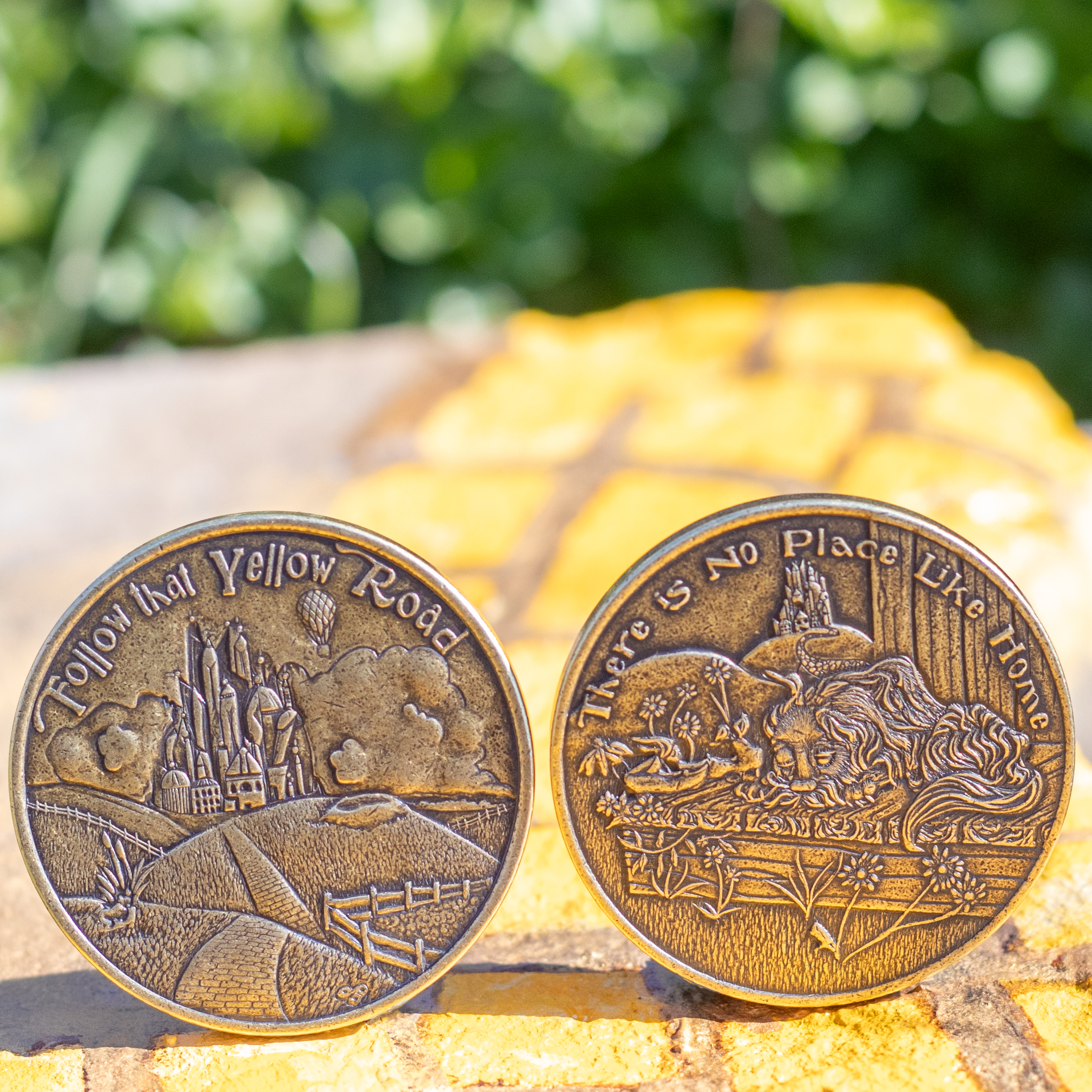 Two brass decision maker coins on painted yellow brick road featuring text, 'Follow that Yellow Road' and 'There is No Place Like Home'