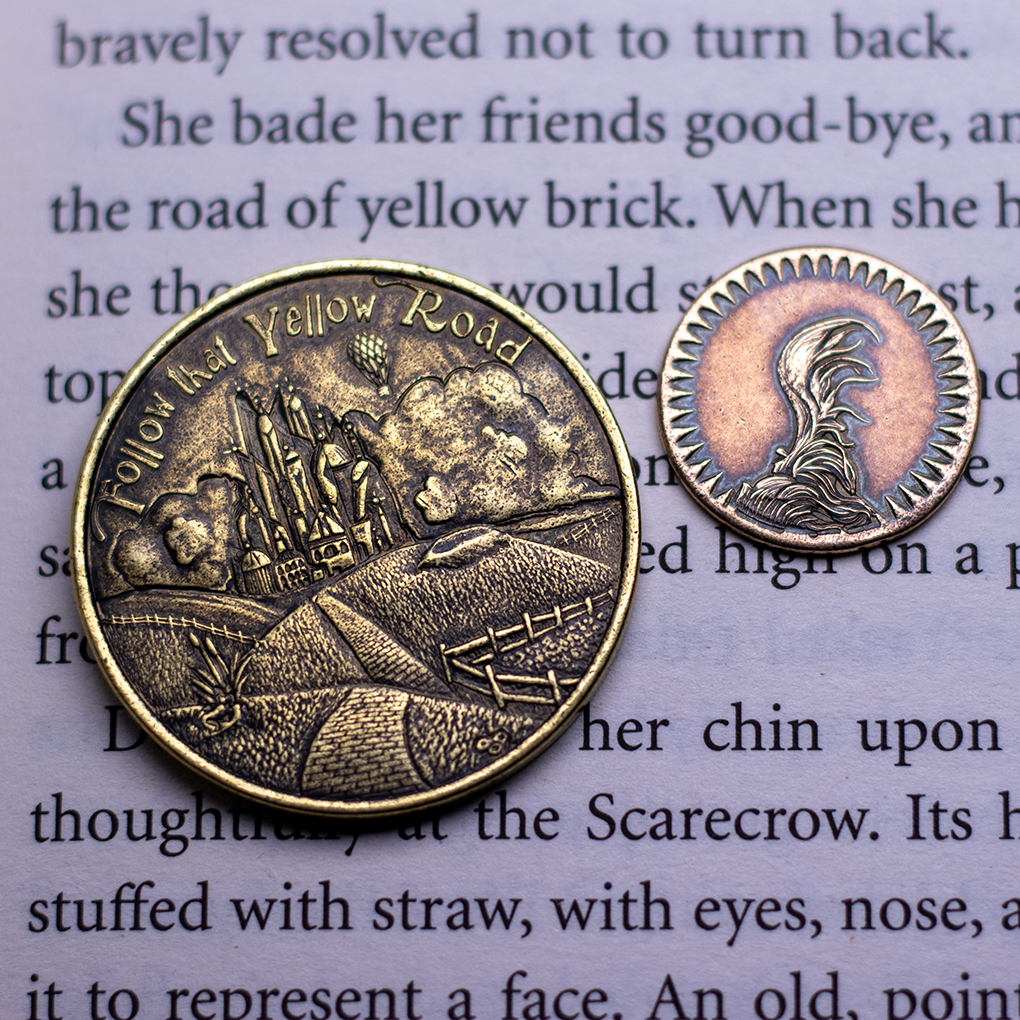 Brass Coin with text, 'Follow that Yellow Road' depicting Baum's famous yellow brick road leading up to the Emerald City displayed against a book page