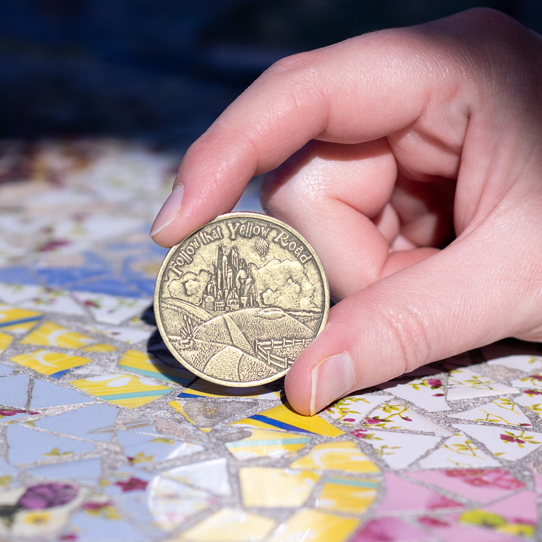 Hand holding brass decision maker coin with text 'Follow that Yellow Road' 