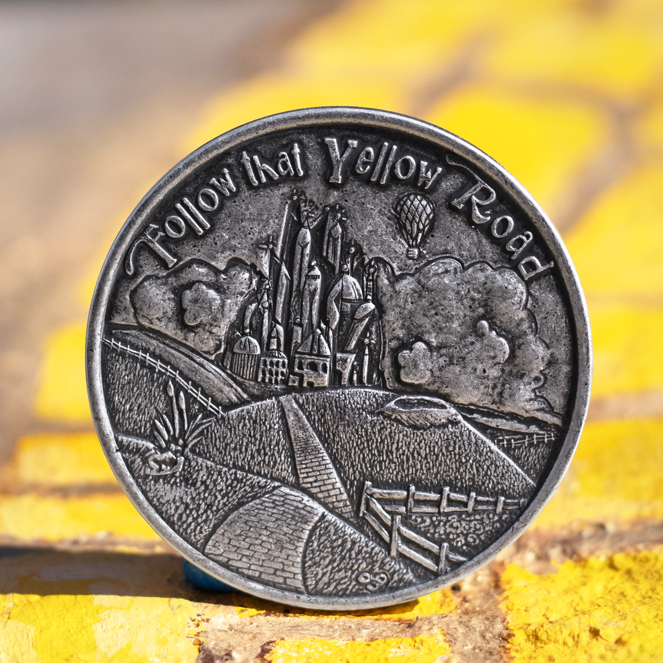 Fine silver coin with text, 'Follow that Yellow Road' depicting the Emerald City from the Wizard of Oz, displayed on a background of hand painted yellow bricks