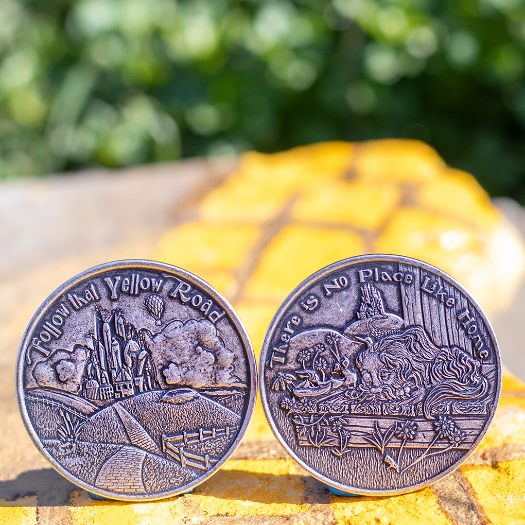 Two silver Dorothy Decision Maker coins displayed on painted yellow brick road